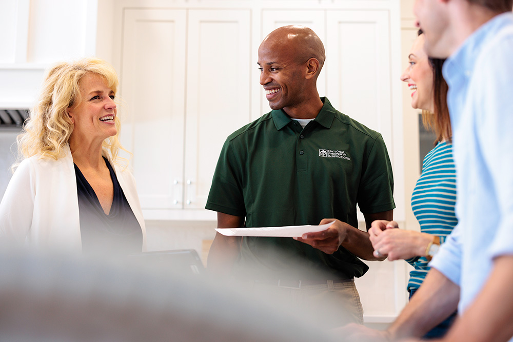 An NPI inspector holds an inspection report while speaking with a real estate agent and two clients.